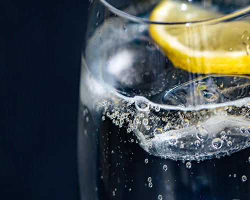 A glass of water with a lemon slice next to an office laptop